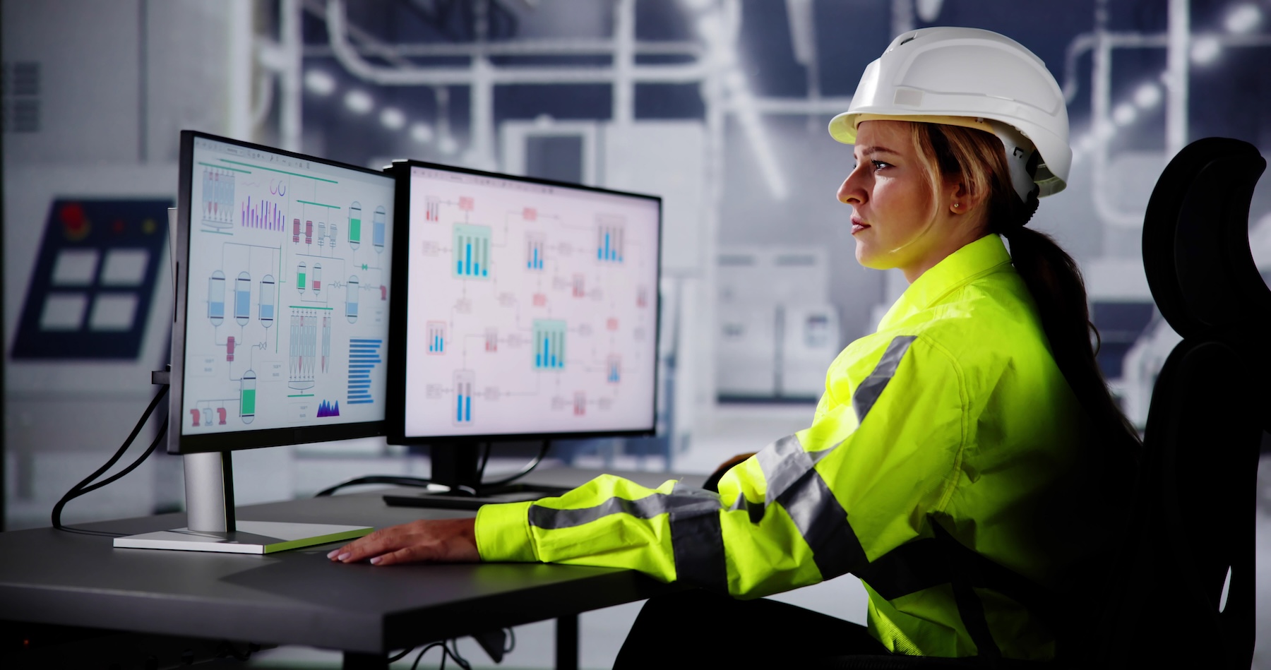 Engineer in a high-visibility jacket analyzing data on multiple computer monitors in a digital control center.