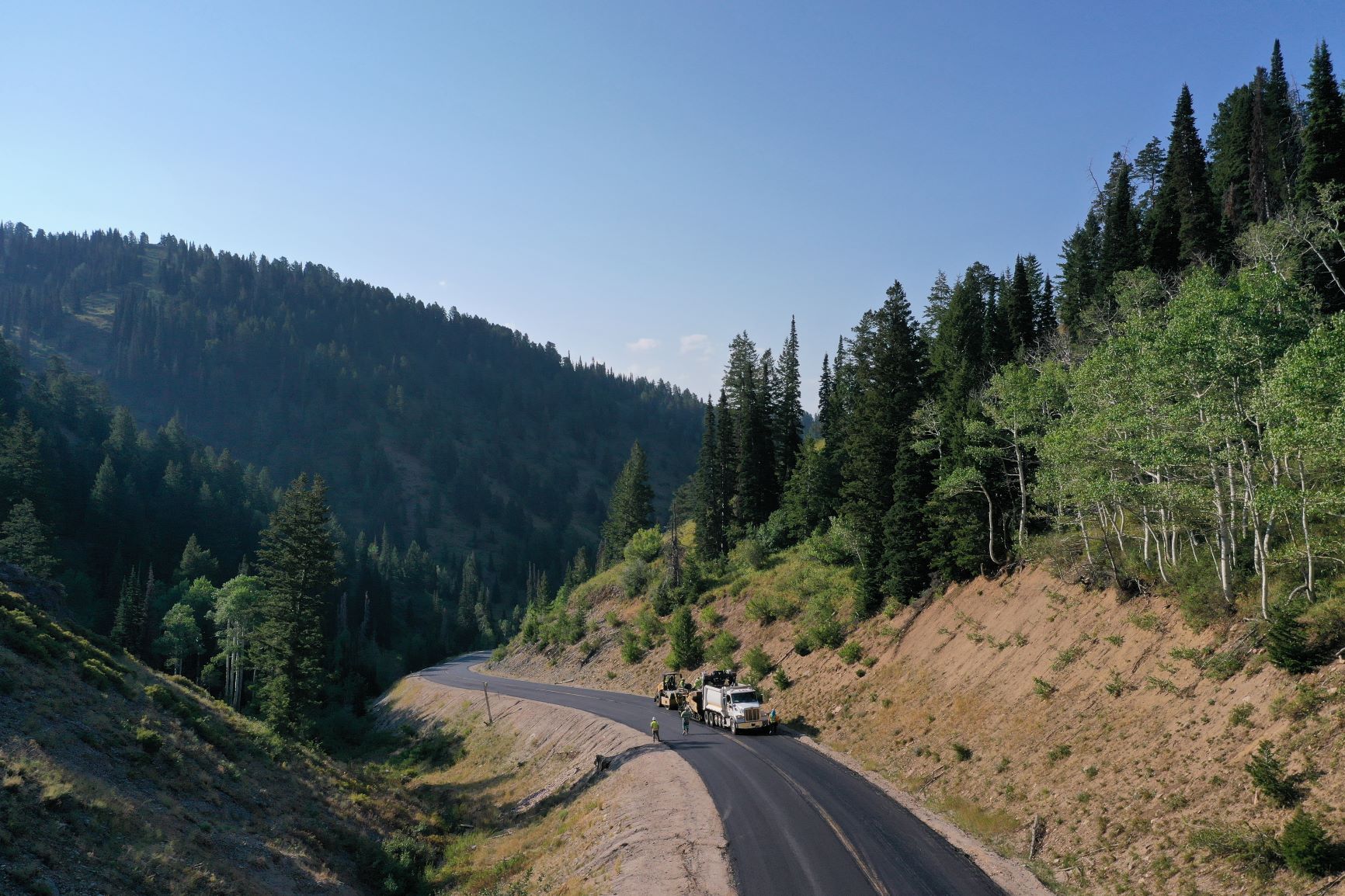 Winding highway through forested mountains near Colorado Springs, Colorado, with a clear blue sky overhead.